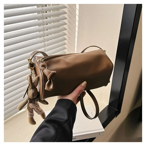 Detailed view of a brown cylinder bag featuring a bow decor and a rabbit plush charm