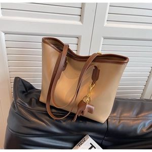 Detail of a large beige tote bag with brown trim and elephant charm on a sofa
