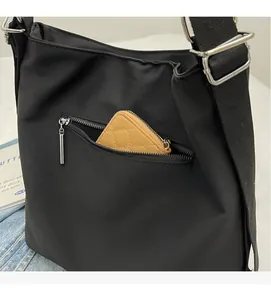 Detail of black nylon tote bag featuring front zipper pocket and adjustable strap buckle