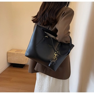 Detail of black leather tote bag featuring gold hardware and minimalist logo pendant