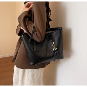 Close-up of a black leather tote bag with gold charms and long shoulder straps
