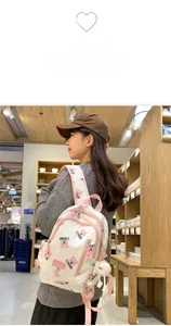 Close-up of white canvas backpack featuring pink cartoon bear print and plush accessory