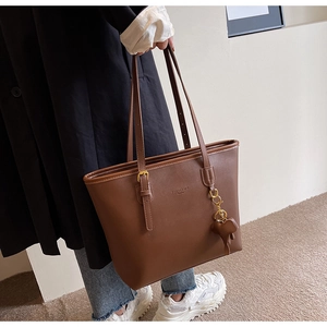 Detail of brown tote bag featuring matte PU leather, bear charm, and adjustable strap