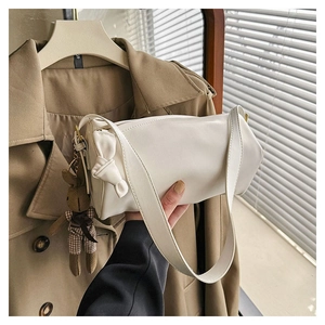 Detail of white cylindrical shoulder bag with bow decor and a teddy bear plush charm