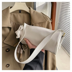 Detail of creamy white cylinder bag featuring a chic bow and gold metal hardware