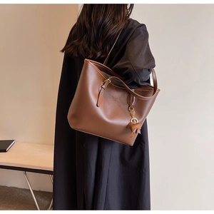 Brown large capacity tote bag with elephant charm shown on shoulder for commute style