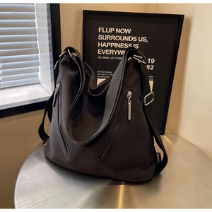 Detail of a black hobo bag with silver zipper and wide strap on a metal table