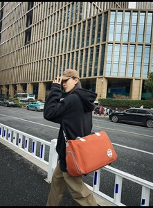 Détail du sac de voyage orange montrant le compartiment latéral et la bandoulière
