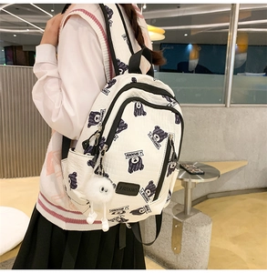 Side view of white backpack with black bear prints and a cute plush monster charm
