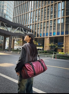 Outdoor shot of a burgundy waterproof nylon travel tote bag held by a model