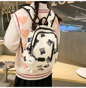 Close-up of a white backpack with bear patterns and plush charm in a trendy urban setting