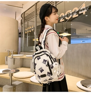 Detailed close-up of bear-print fabric and plush ball charm on a cream white backpack