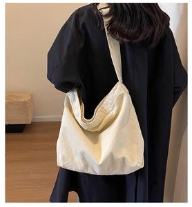 Detail of a large off-white canvas tote bag worn by a model in a minimal indoor setting