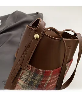 Close-up of retro bucket bag with brown leather, red plaid tweed and gold ball clasp