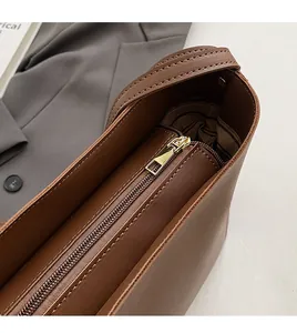 Macro detail of gold metal zipper closure on brown leather plaid shoulder bag
