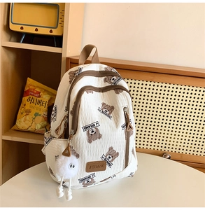 Close-up of white backpack with brown bear prints and a cute plush ball keychain accessory