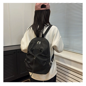 Close-up of black nylon backpack featuring a drawstring front pocket and dual zippers