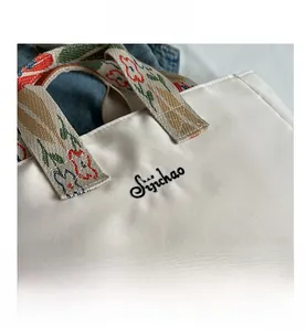 Dettaglio della borsa tote bianca con manici ricamati a fiori e logo del marchio Sijichao