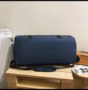 Detail of dark blue Oxford travel bag with adjustable padded shoulder strap on wooden tray