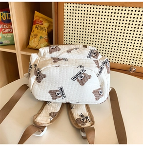 Detail of white quilted backpack featuring brown bear print and adjustable straps