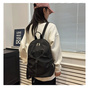 Model wearing a large black nylon backpack with drawstring pocket and silver zippers