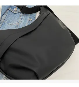 Detail of soft matte black nylon crescent crossbody bag styled with a denim jacket