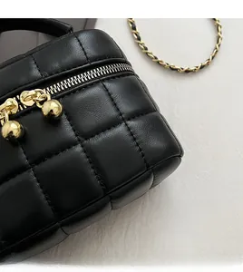 Close-up of quilted black leather texture with gold sphere zipper and chain strap