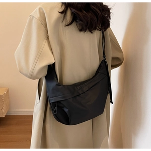 Detail view of the black nylon crescent bag worn crossbody over a stylish trench coat