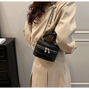 Detail of black quilted leather mini bucket bag with gold chain strap and ball pendant