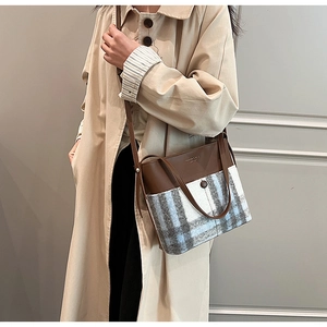 Detail of plaid tweed and brown leather bucket bag worn with a chic beige coat