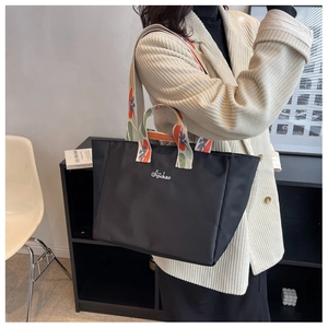 Vista laterale di borsa tote in nylon nero con tracolla a motivi colorati e ricamo sulla borsa