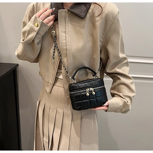 On-body shot of a black quilted bucket bag featuring a gold chain strap and top handle