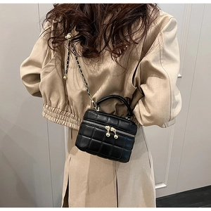 Detail of black quilted bucket bag featuring a gold ball charm and chain strap