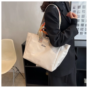 Dettaglio della borsa tote in nylon bianco sporco con tracolla ricamata indossata a spalla