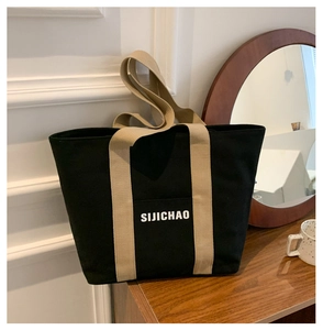 Detail of black canvas tote bag with SIJICHAO print and beige handles on wooden table