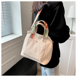 Detail of off-white nylon tote bag showing floral strap and front snap pocket