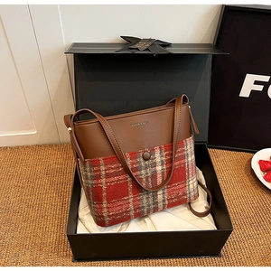 Detail of plaid fabric and brown leather bucket bag with golden fashion logo lettering