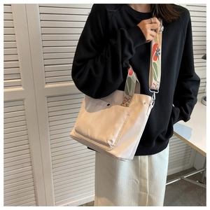 Detail of cream nylon tote bag featuring a colorful floral embroidered wide shoulder strap