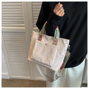 Detail of cream tote bag featuring a floral patterned wide shoulder strap and front pocket