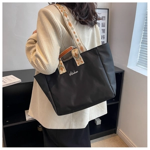 Vista laterale di una borsa tote nera in nylon con tracolla etnica indossata dal modello