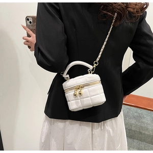 Detail of white quilted cube bag featuring gold chain strap and spherical metal zipper pull