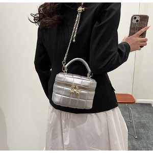 Close-up of silver quilted vanity bag with chain strap worn by a model in casual outfit