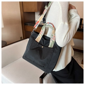 Detail of a black nylon tote bag with vibrant floral embroidered handles and shoulder strap