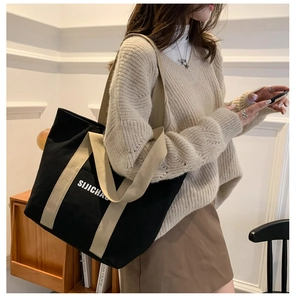 Close-up of black canvas tote bag with beige handles and minimalist white lettering