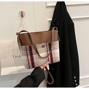 Detail of brown leather and red plaid wool stitching on a stylish bucket handbag