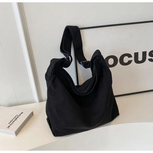 Detail of a large black canvas hobo bag with a wide adjustable shoulder strap on a white table