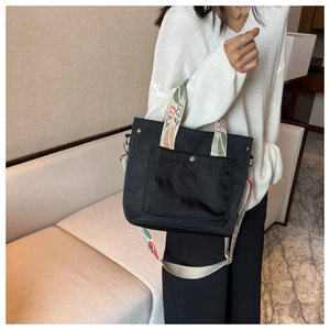 Detail of black nylon tote bag featuring colorful floral shoulder strap and metal snap pocket
