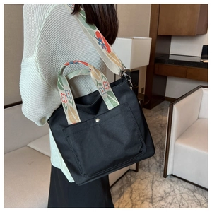 Detail showing colorful floral embroidered strap and black nylon tote bag on a model
