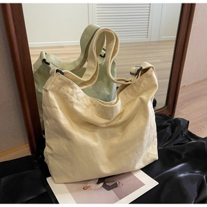 Close-up of beige canvas tote bag with adjustable black shoulder strap on leather surface