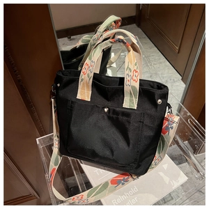 Detail of black nylon tote bag with floral pattern straps and metal snap front pocket